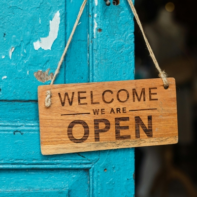 blaue Tür mit einem Holzschild, auf dem steht "Welcome, we are open"
