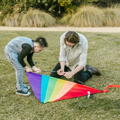 zwei Personen bereiten einen Drachen in Regenbogenfarben zum Fliegen vor